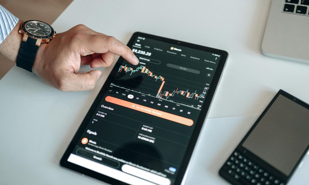 Person pointing at a financial chart on a tablet displaying performance metrics and pricing data