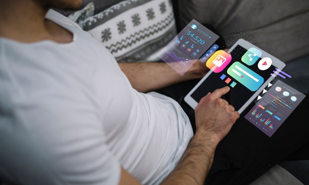 Person on a couch using a tablet with floating user interface elements showing account dashboard, charts, and media icons